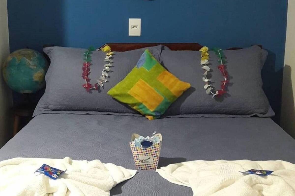 A bed with gray bedding, a colorful pillow, and a small white vase with a polka dot pattern.