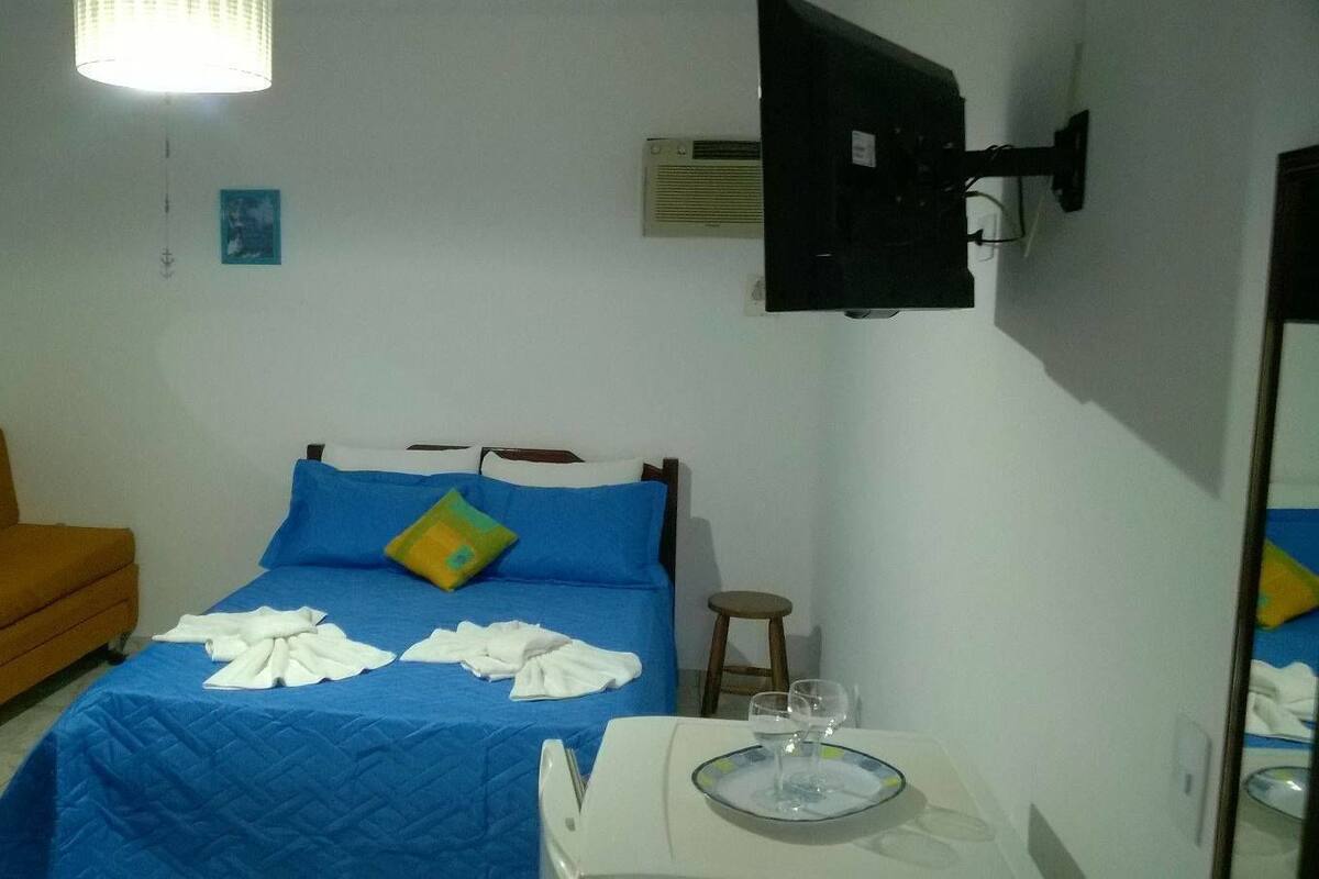 A bedroom with a bed, a chair, a table with glasses, and a wall-mounted TV.