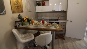A modern kitchen with white cabinets, a wooden countertop, and two white bar stools. - Casa Dell'Artista (Matera)