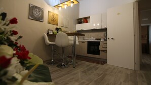 A modern kitchen with white cabinets, a wooden dining table, and two white bar stools. - Casa Dell'Artista (Matera)