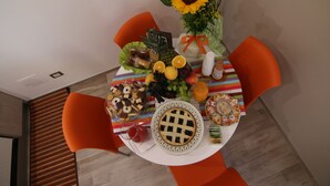 A dining table with a variety of food items, including fruits, vegetables, and cookies, surrounded by orange chairs. - Casa Dell'Artista (Matera)