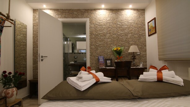 A hotel room with a bed, two pillows, a desk with a lamp, a vase with flowers, and a painting on the wall. - Casa Dell'Artista (Matera)