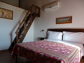 A bedroom with a wooden staircase, a bed with white linens, and two paintings on the walls. - Agriturismo Podere 1248 (Ladispoli)