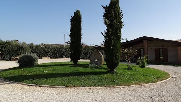 A well-maintained garden with two tall cypress trees, a stone sign, and a building with a tiled roof. - Agriturismo Podere 1248 (Ladispoli)