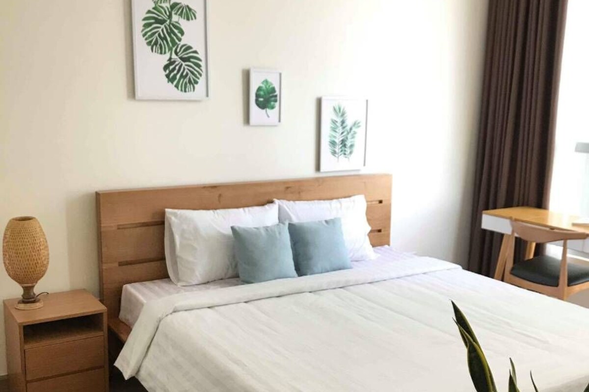 A neatly arranged hotel room with a wooden bed, white bedding, and a small bedside table with a lamp.