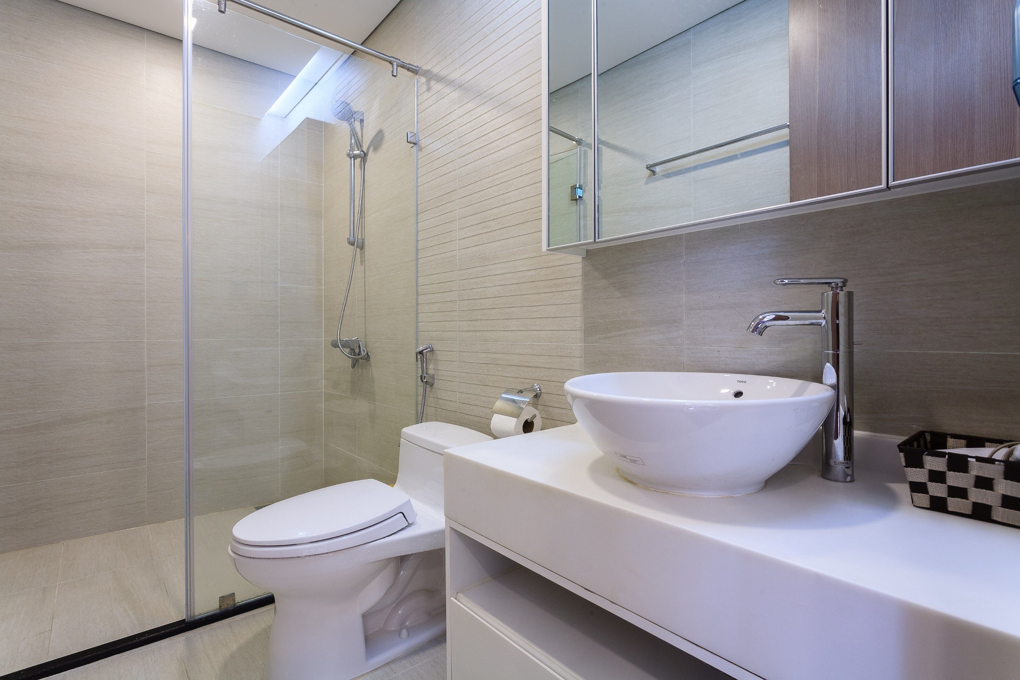 A modern bathroom with a glass shower enclosure, a white toilet, and a white sink with a checkered basket beside it.