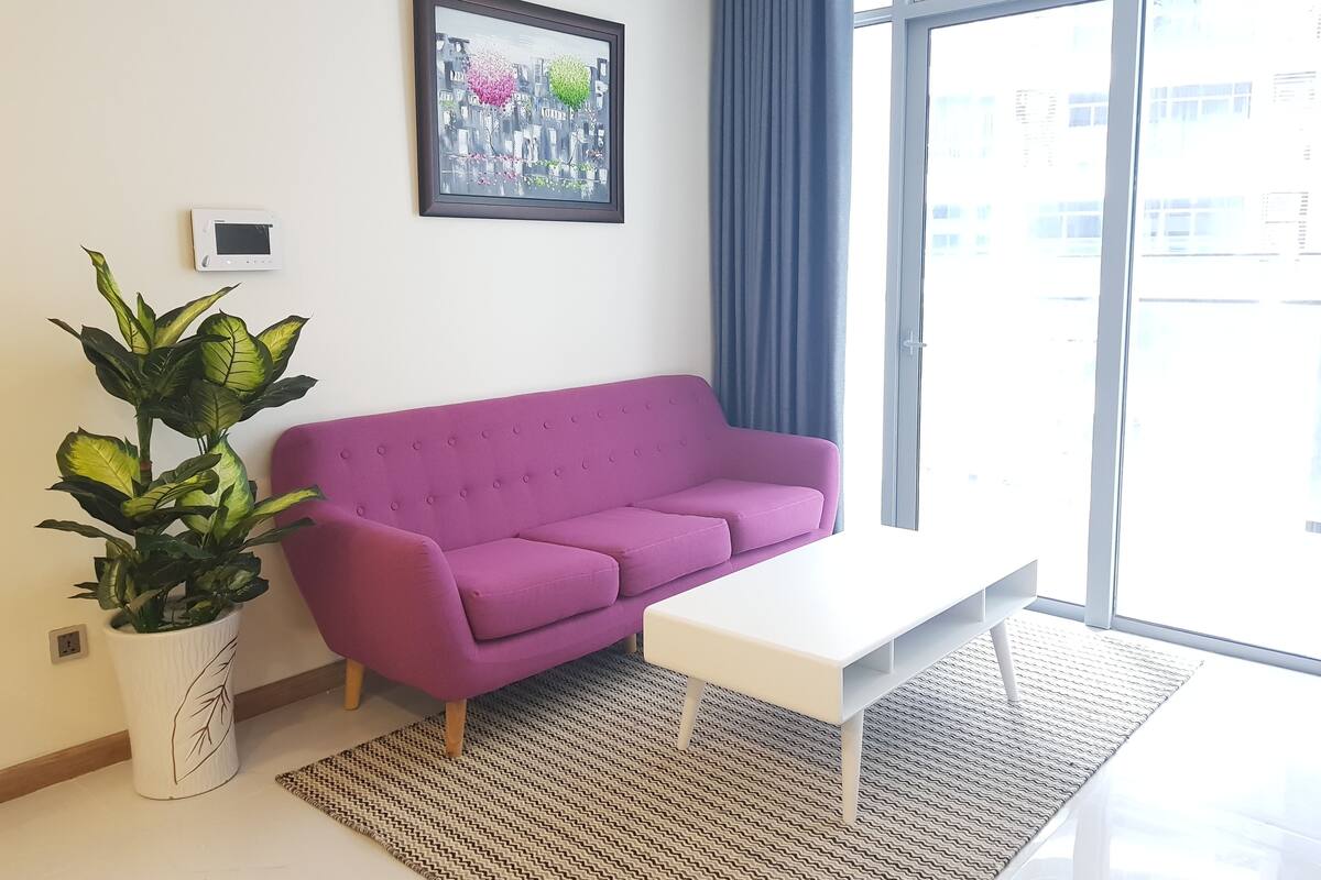 A modern living room with a purple sofa, a white coffee table, and a large window with a view of buildings.