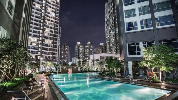 A nighttime swimming pool area surrounded by high-rise buildings with a view of the city skyline. - The Berry Vinhomes Luxury Apartments (Ho Chi Minh City)