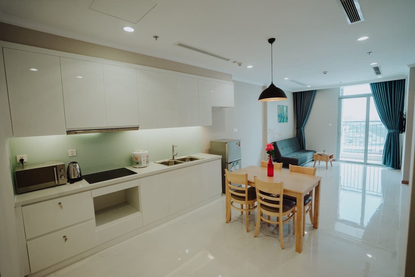 A modern kitchen with white cabinets, a dining area with wooden chairs, and a large window with curtains.