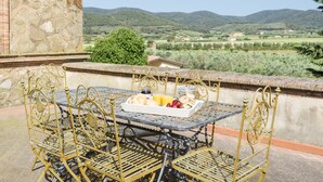 A metal table with a tray of food and chairs on a terrace with a view of green hills. - Fattoria Pian di Rocca (Castiglione della Pescaia)