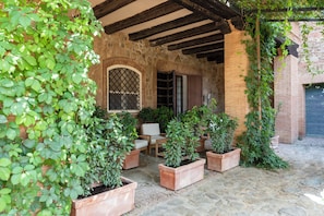 A stone building with a wooden ceiling, a window with a metal grille, and several potted plants. - B&B Terre di Castiglione già Fattoria Pian di Rocca (Castiglione della Pescaia)