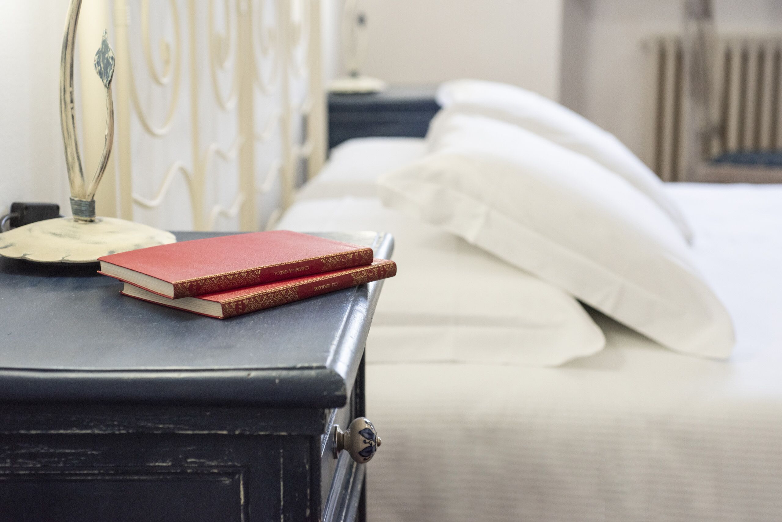 Un lit avec du linge de lit blanc, une table de chevet avec une lampe et deux livres.