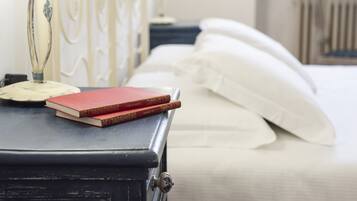 Un lit avec du linge de lit blanc, une table de chevet avec une lampe et deux livres.
