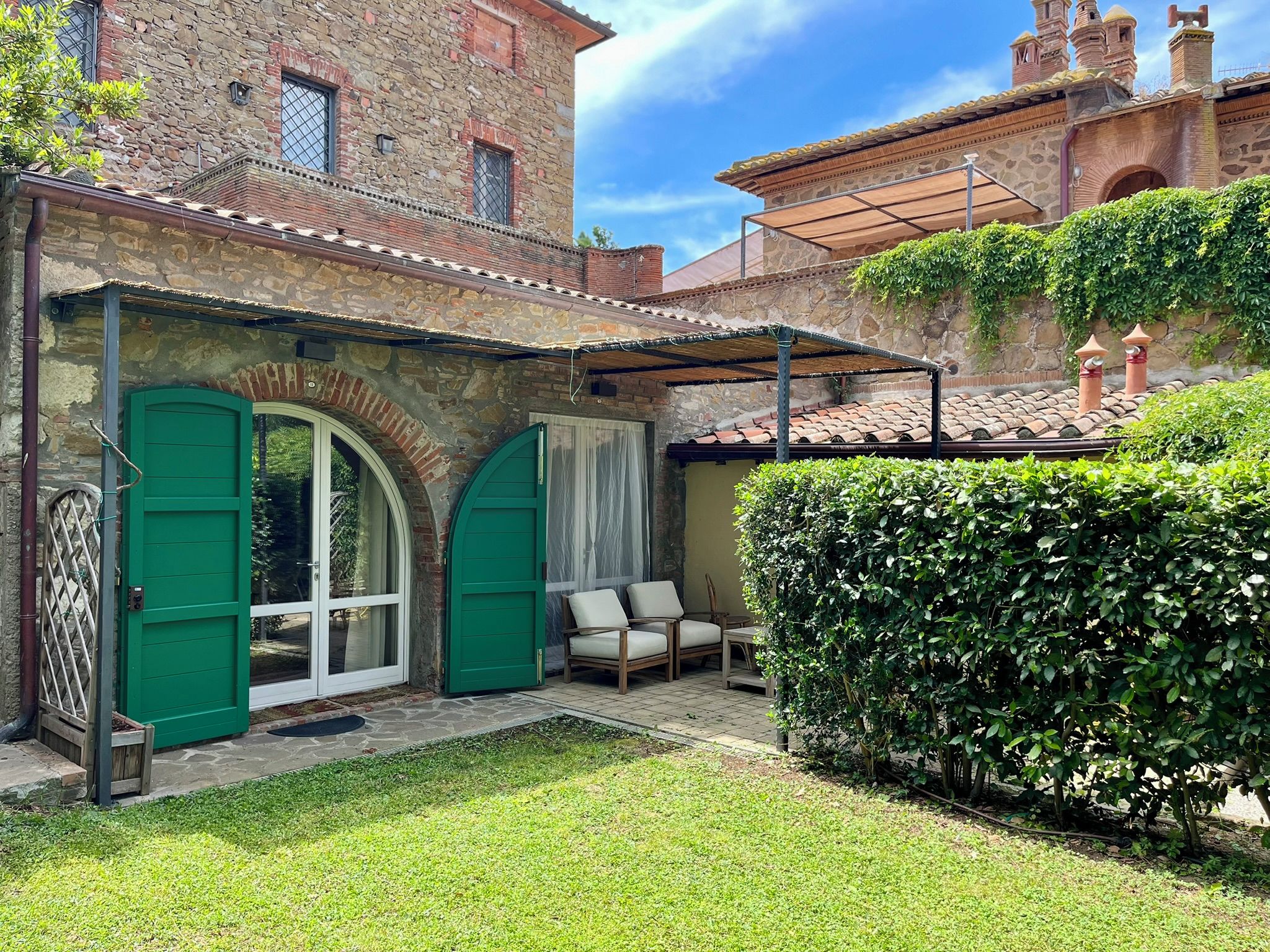 Une cour avec un espace de repos abrité, une porte verte et un bâtiment en pierre en arrière-plan.