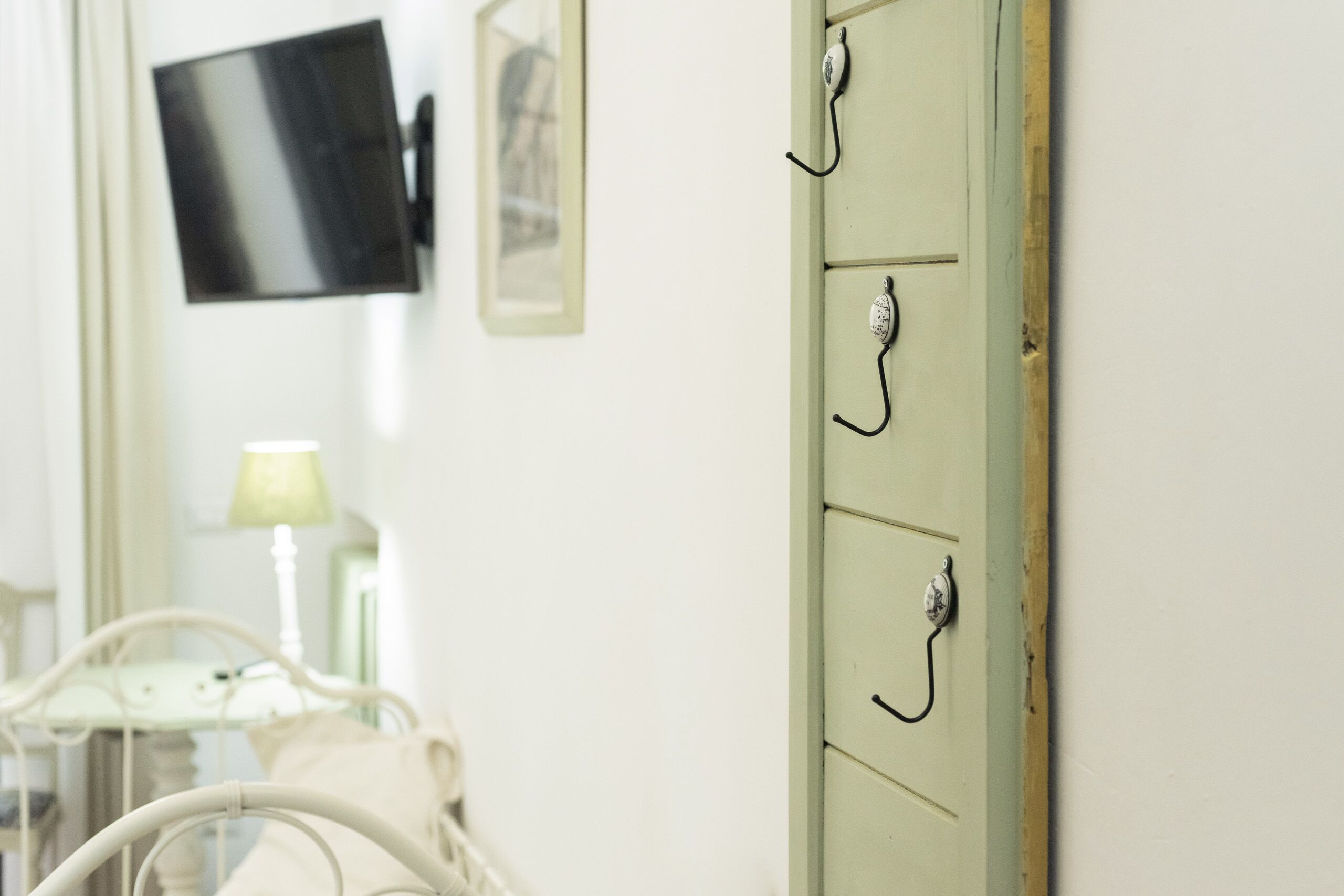 A room with a bed, a television mounted on the wall, and a cabinet with hooks.