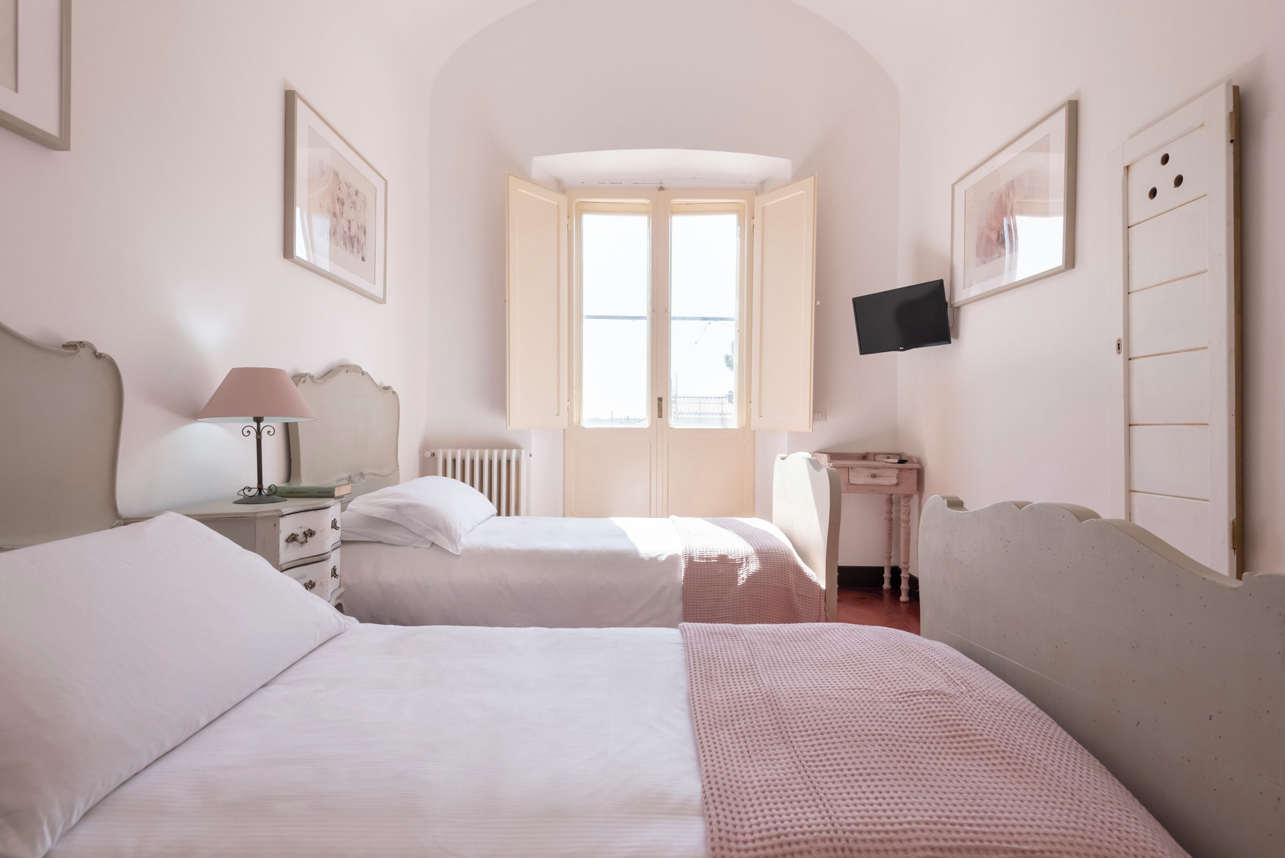 A room with two beds, a desk, a chair, a radiator, and a television on the wall.