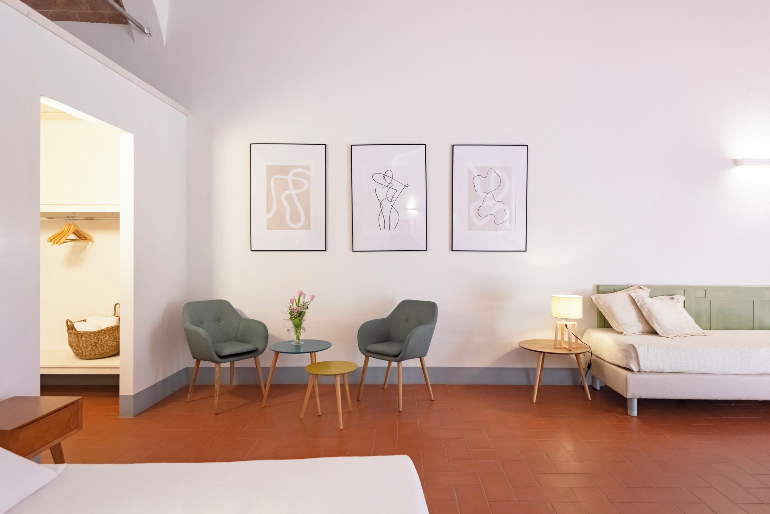Une chambre d’hôtel moderne, équipée d’un lit, de deux fauteuils, d’une petite table et d’un canapé. Trois œuvres d’art encadrées ornent le mur.