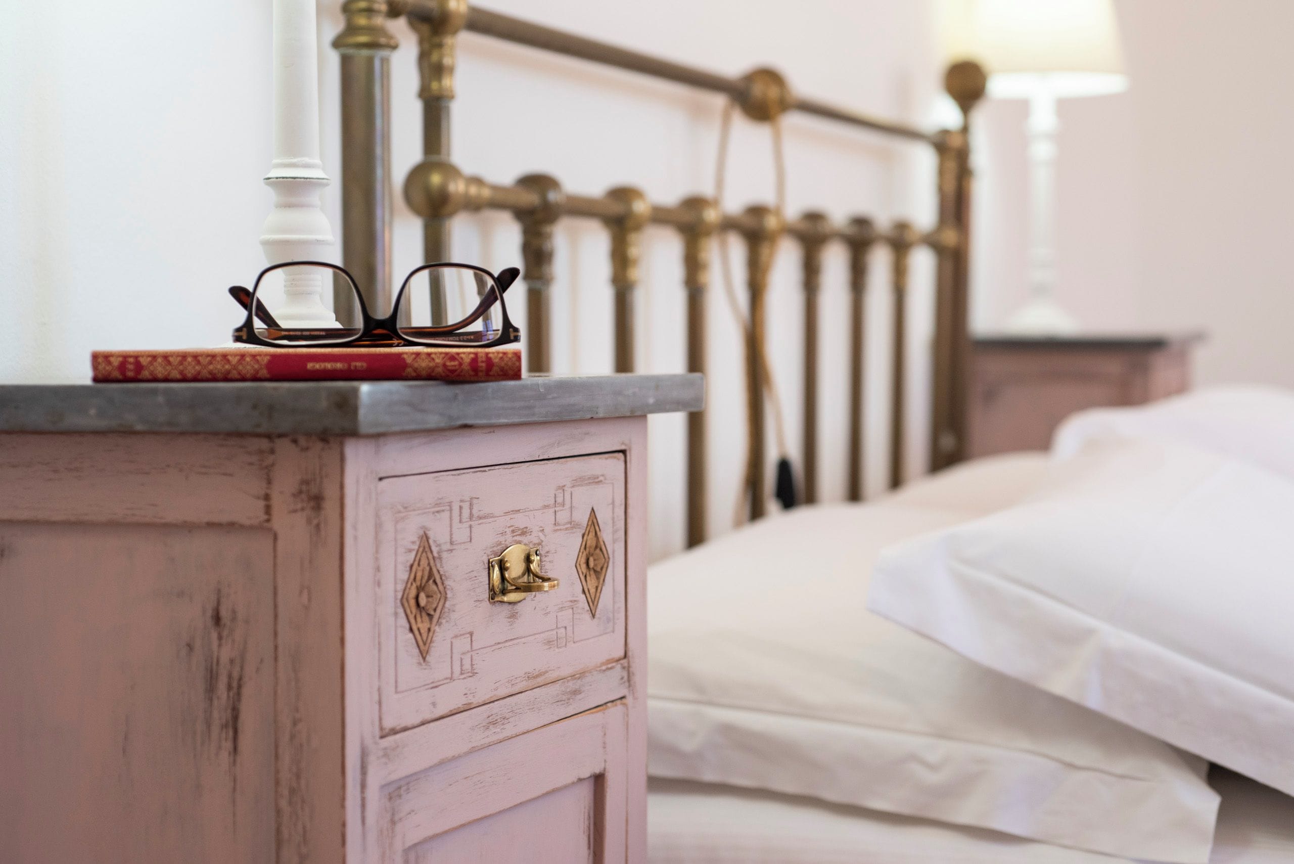 Un lit avec du linge de lit blanc, une table de chevet avec une lampe et une tête de lit décorative en métal.