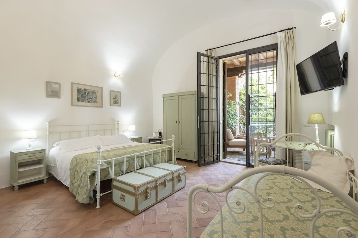 A bedroom with a bed, a wardrobe, a suitcase, a television, and a window with curtains.