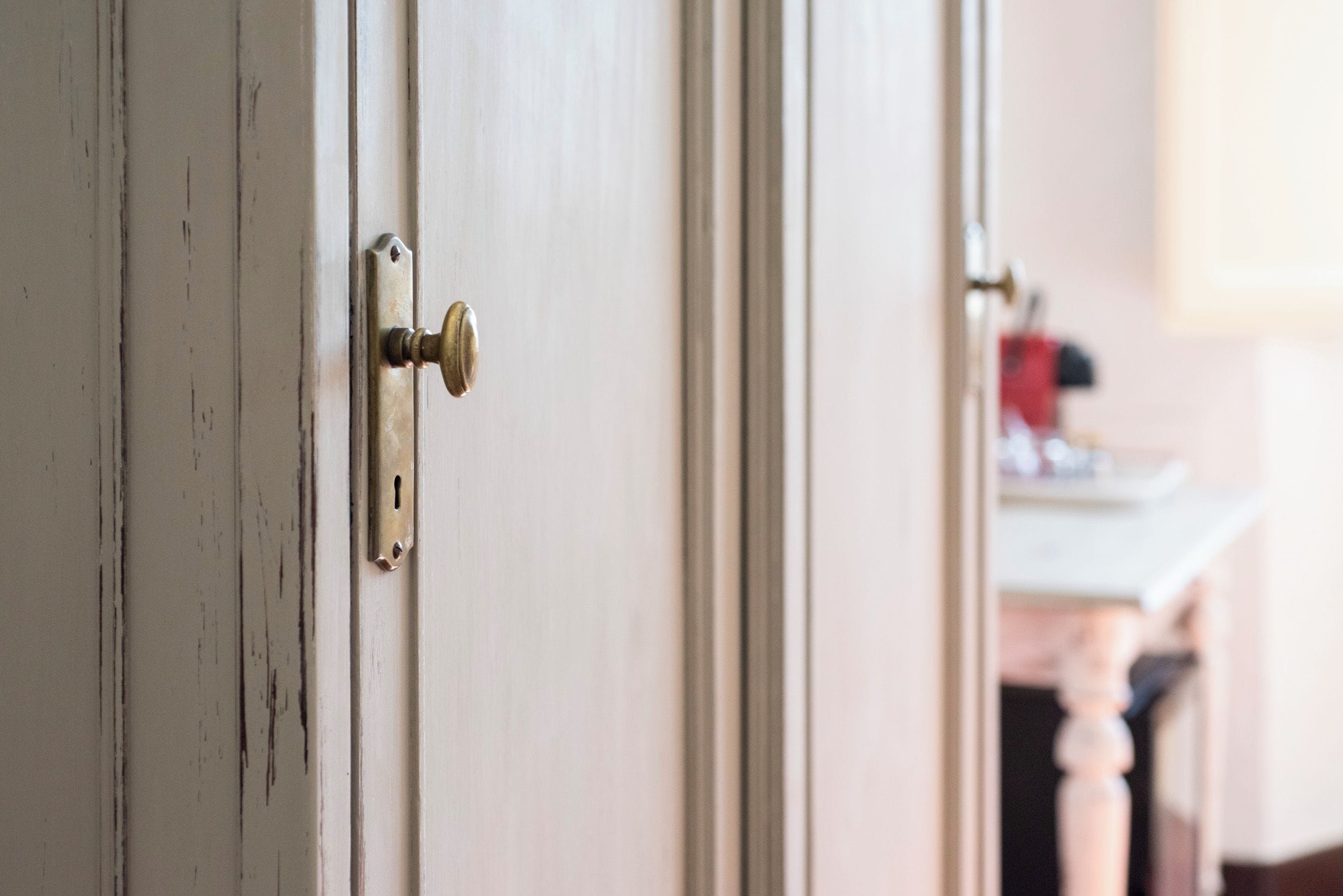 A door with a brass handle and a keyhole, leading to a room with a white countertop and a red object on it.