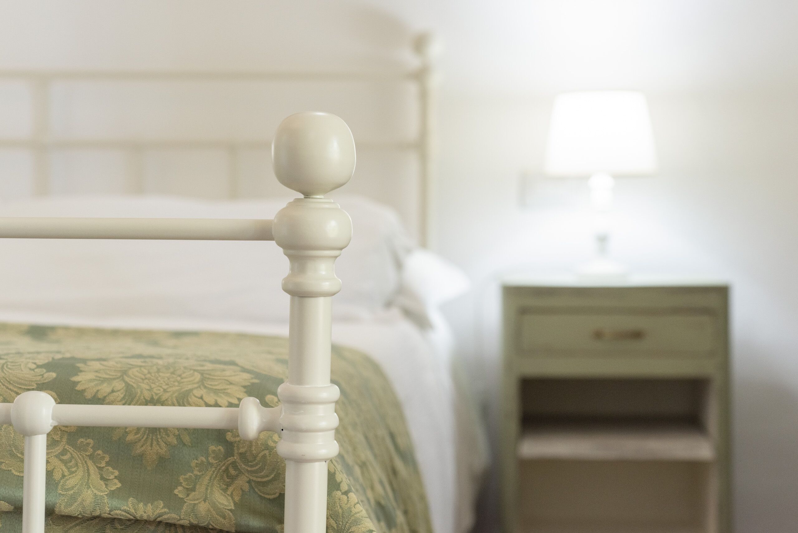 A bed with a wooden headboard, a nightstand with a lamp, and a green patterned bedspread.
