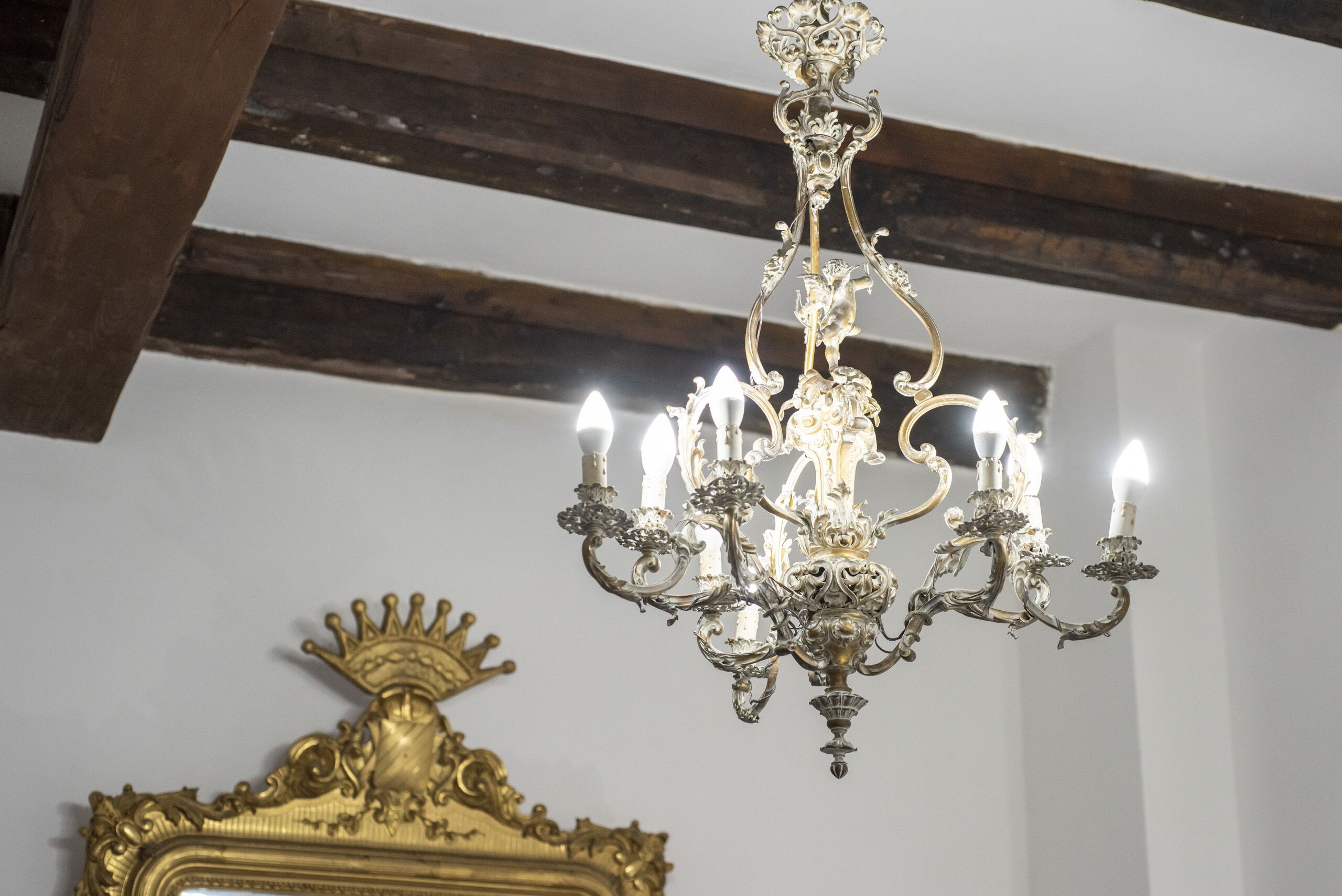 Un lustre doté de plusieurs lampes en forme de bougies et d’un grand miroir doré orné, surmonté d’un motif de couronne.