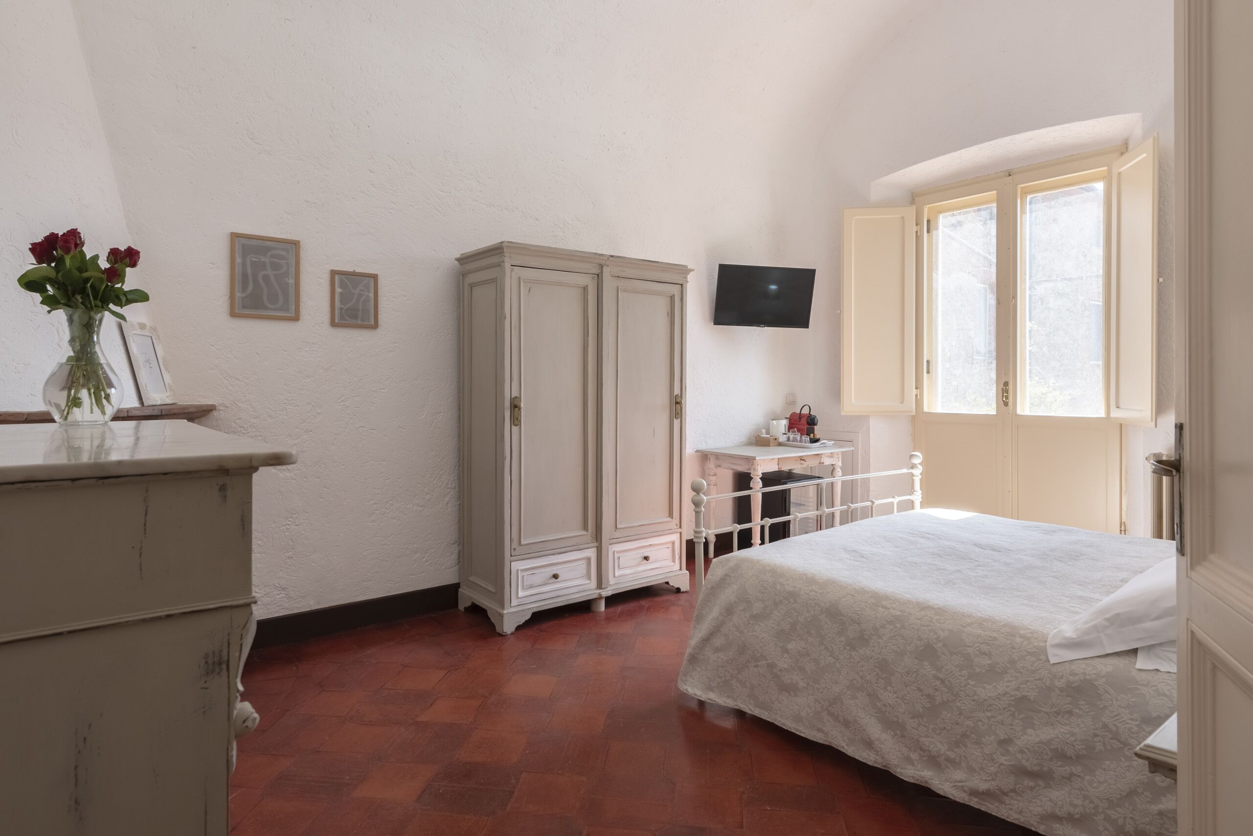 Un dormitorio con cama, armario, una mesita, televisor y ventana.
