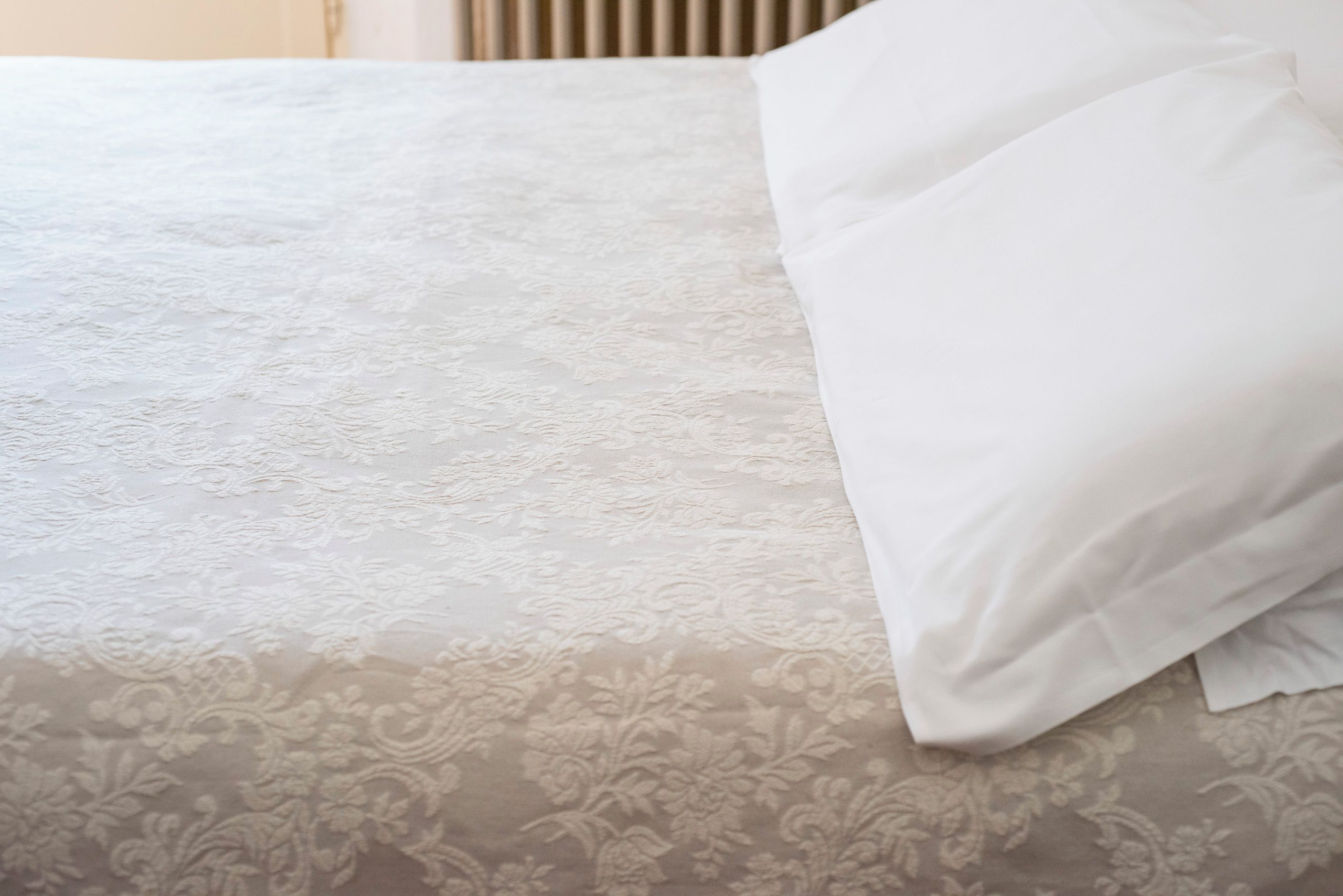Ein Bett mit einem gemusterten Bettüberwurf und einem weißen Kopfkissen.