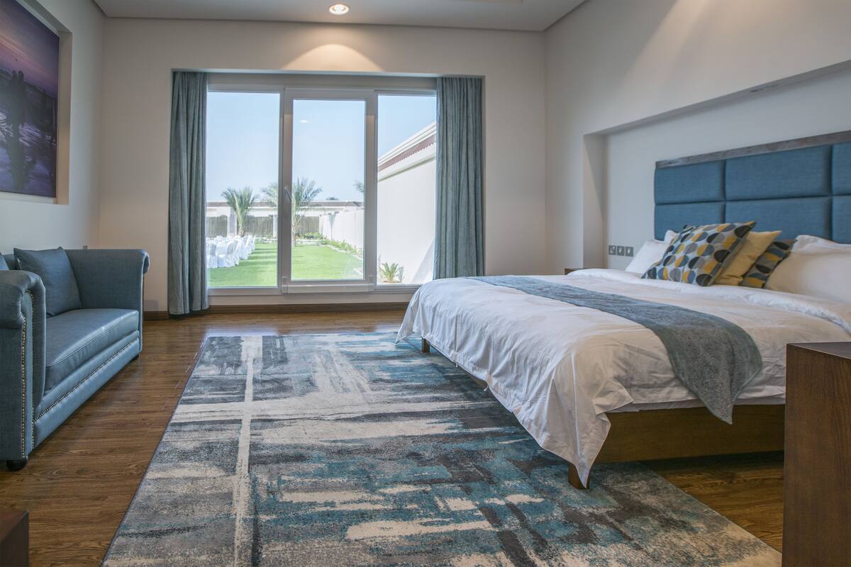 Ein modernes Schlafzimmer mit einem großen Bett, einer Couch und Blick auf einen Garten.