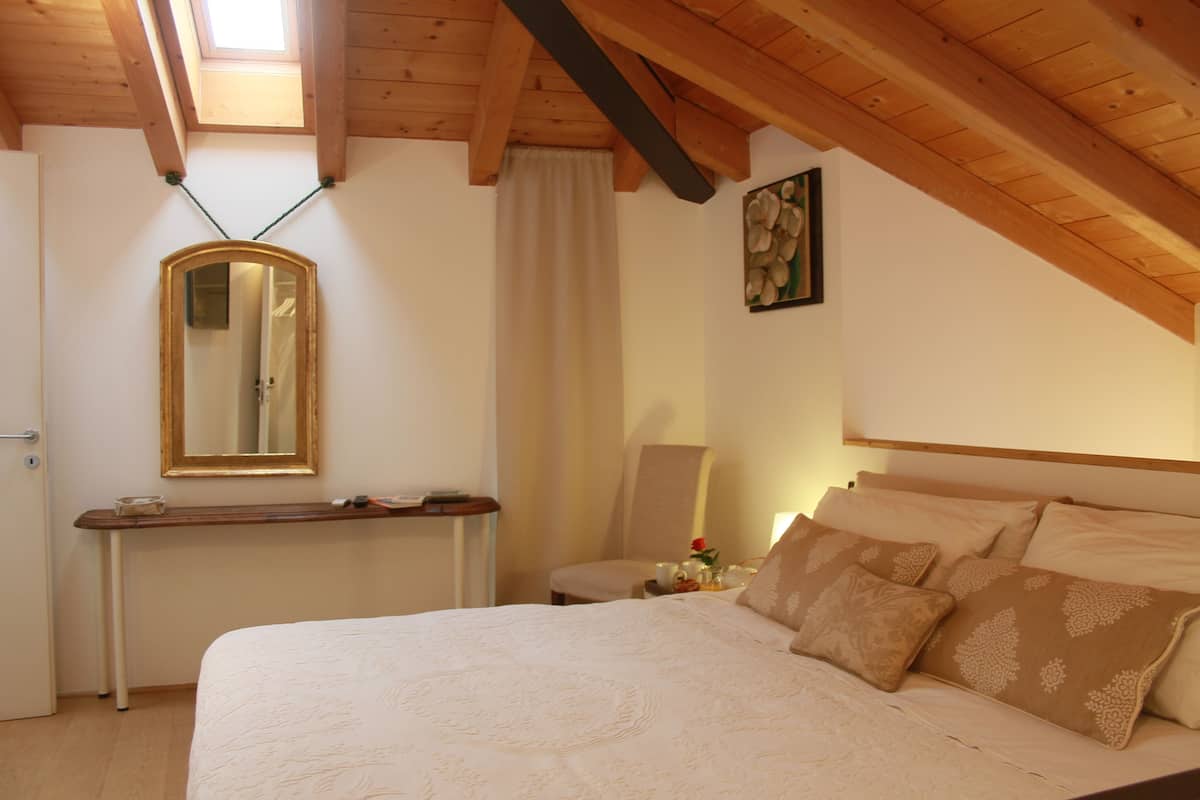 Un dormitorio con una cama grande, una mesita de noche, un espejo, una silla y un cuadro en la pared.