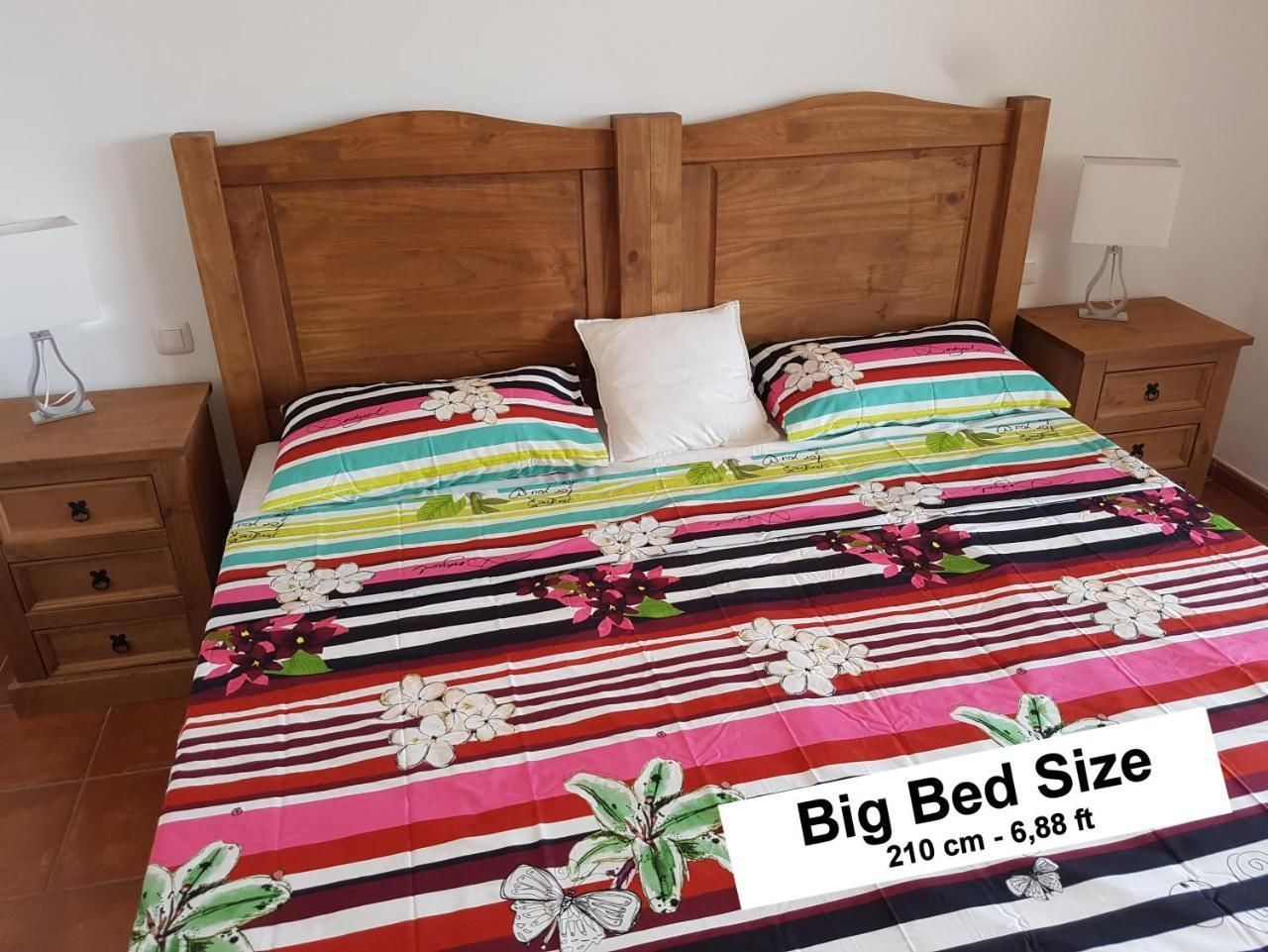 Una cama grande con colcha estampada de flores y rayas, cabecera de madera y mesitas de noche con lámparas.