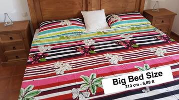 Una cama grande con colcha estampada de flores y rayas, cabecera de madera y mesitas de noche con lámparas.