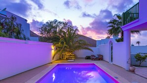 A swimming pool with a sunset view, a covered seating area, and a white building with a green balcony. - Timanfaya Casa Rural (Yaiza)