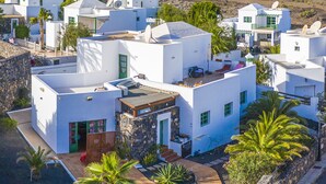 A coastal village with white buildings, palm trees, and a mountain in the background. - Timanfaya Casa Rural (Yaiza)
