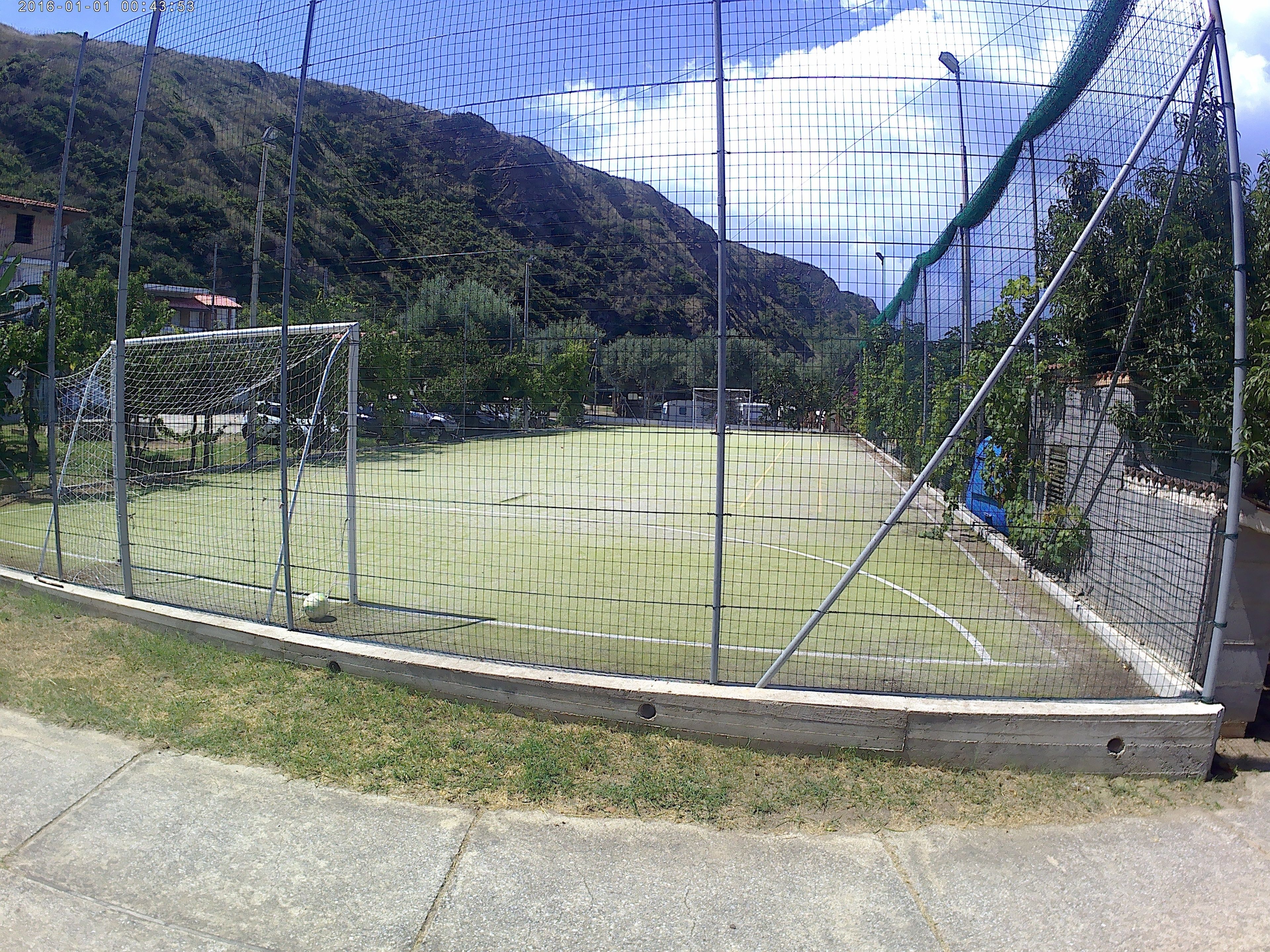 A fenced sports field with a goalpost, surrounded by a mountainous landscape.