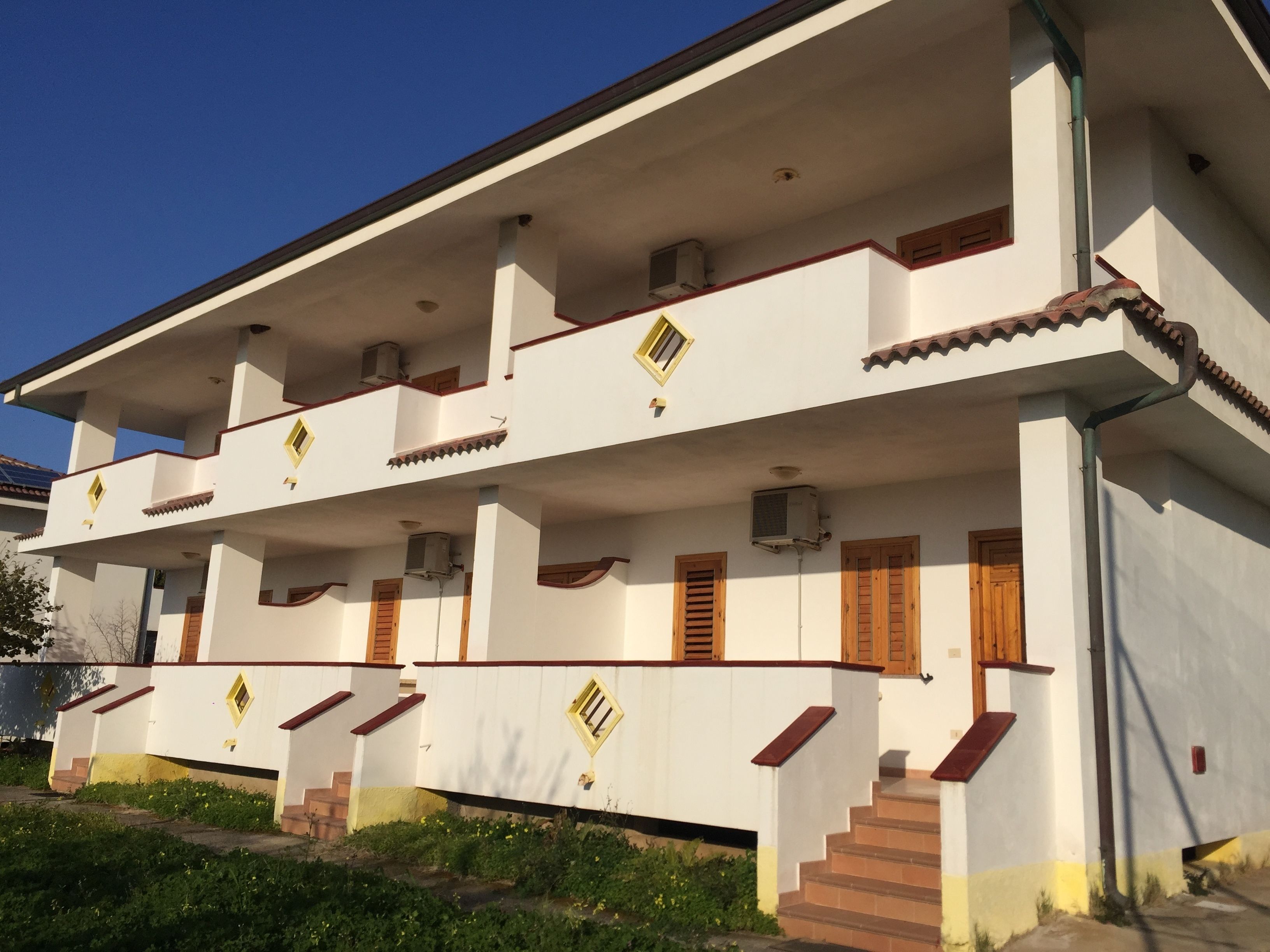 Un immeuble à plusieurs étages, doté d’une façade blanche, de cadres de fenêtres en bois et d’un toit recouvert de tuiles.