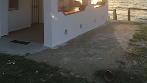 A white building with a covered patio overlooking the sea, featuring a door and windows.