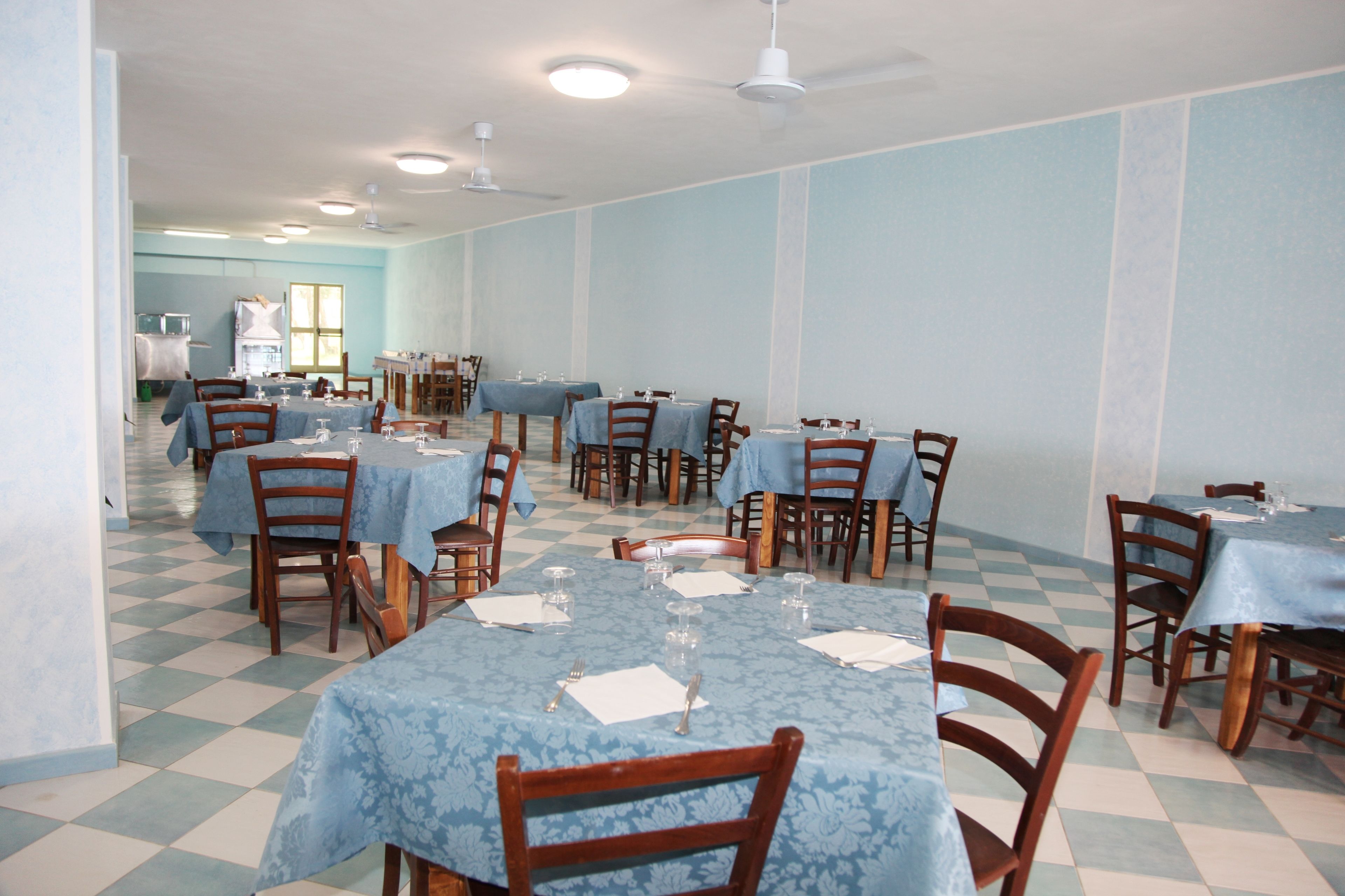 Un comedor con mesas dispuestas para el servicio, sillas y un piso con estampado de cuadros.