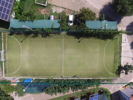 Vista aérea de un campo deportivo con valla, paneles solares y un coche aparcado.