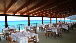 An outdoor restaurant with tables and chairs, overlooking the sea.
