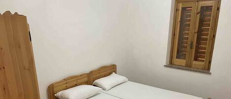 A double bed with wooden headboard and footboard, two white pillows, and a nightstand with a lamp.