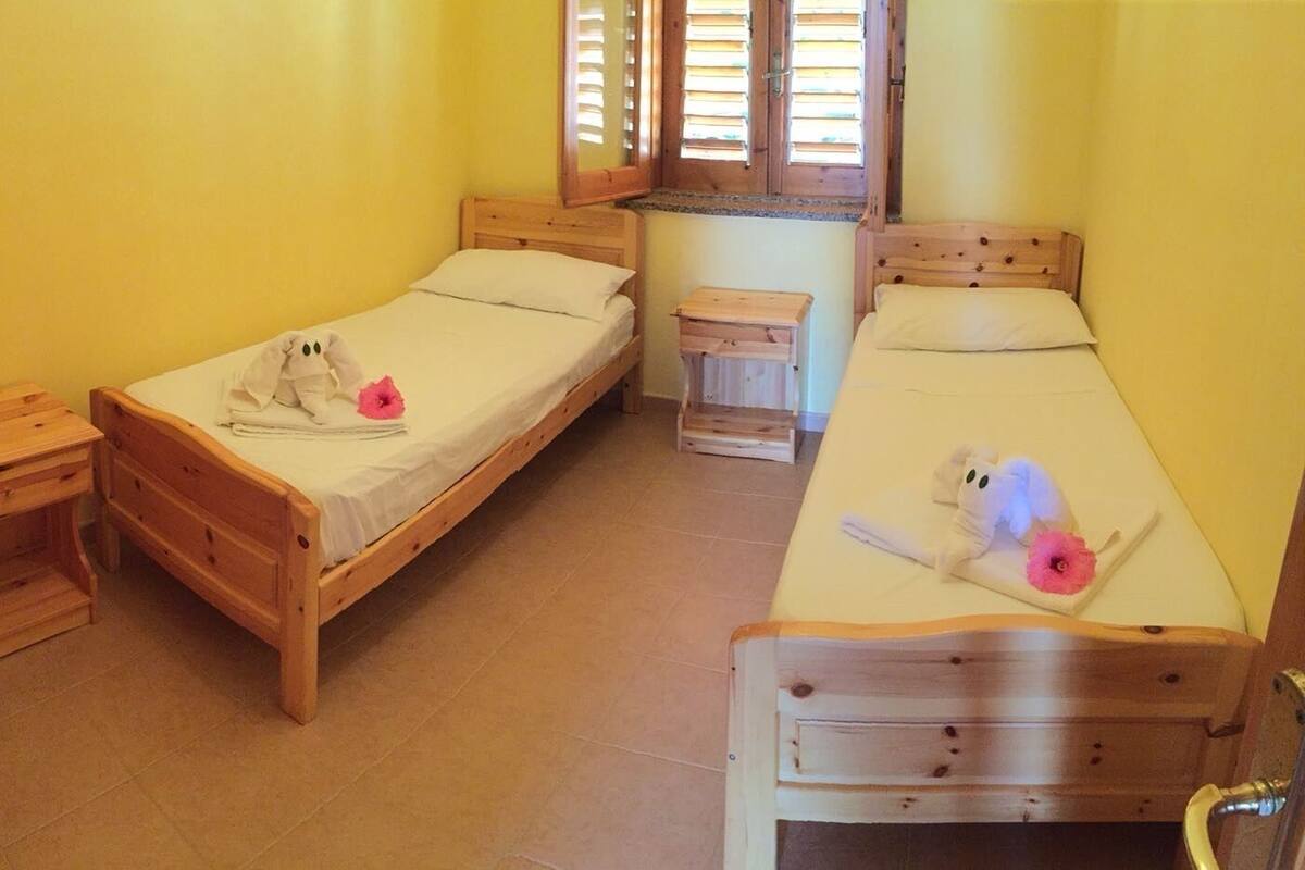 Une chambre avec deux lits en bois, une petite table de chevet en bois avec une lampe, et une fenêtre avec des volets en bois.