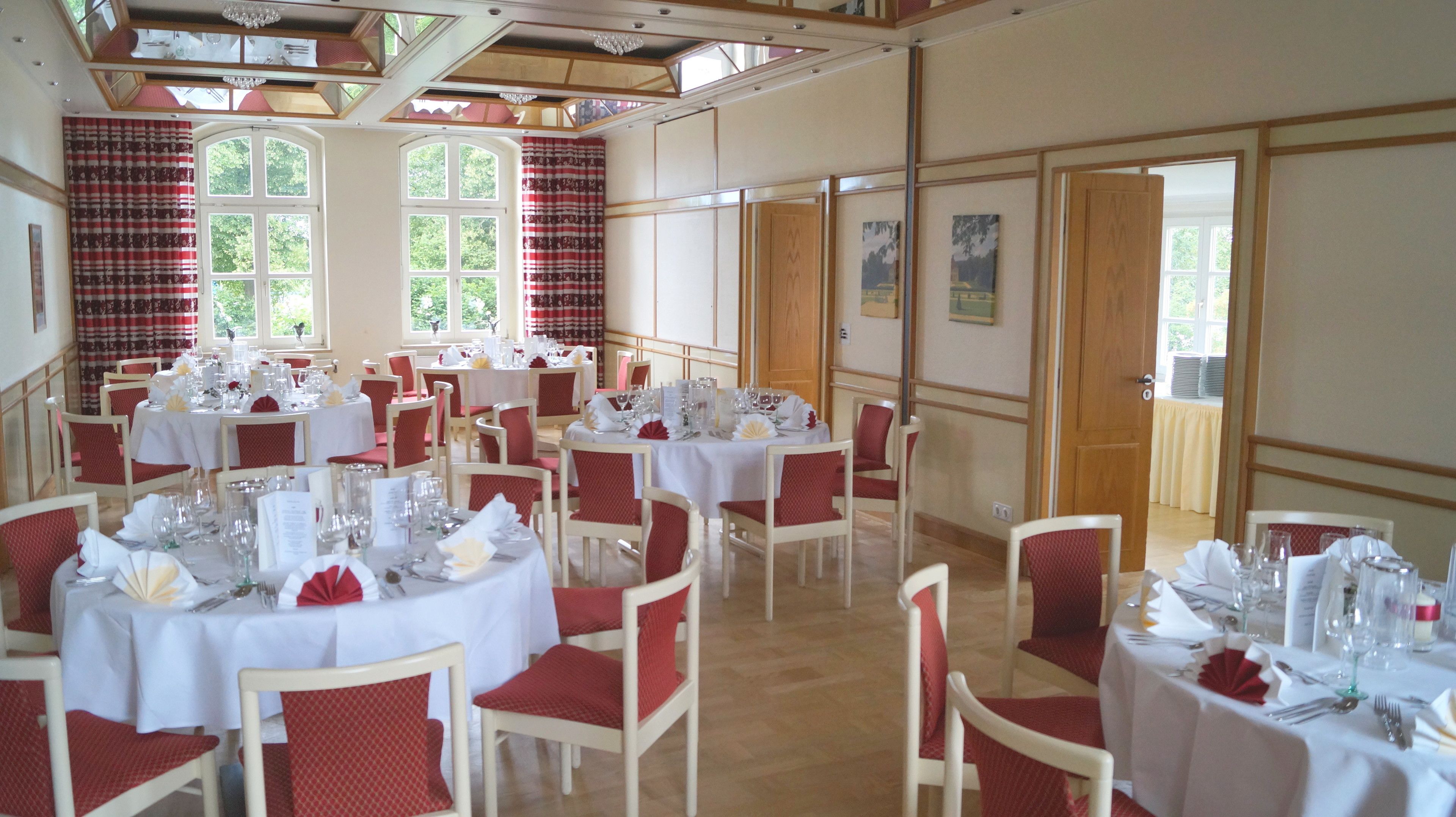 A dining area with round tables set for multiple guests, featuring white tablecloths and red chairs.