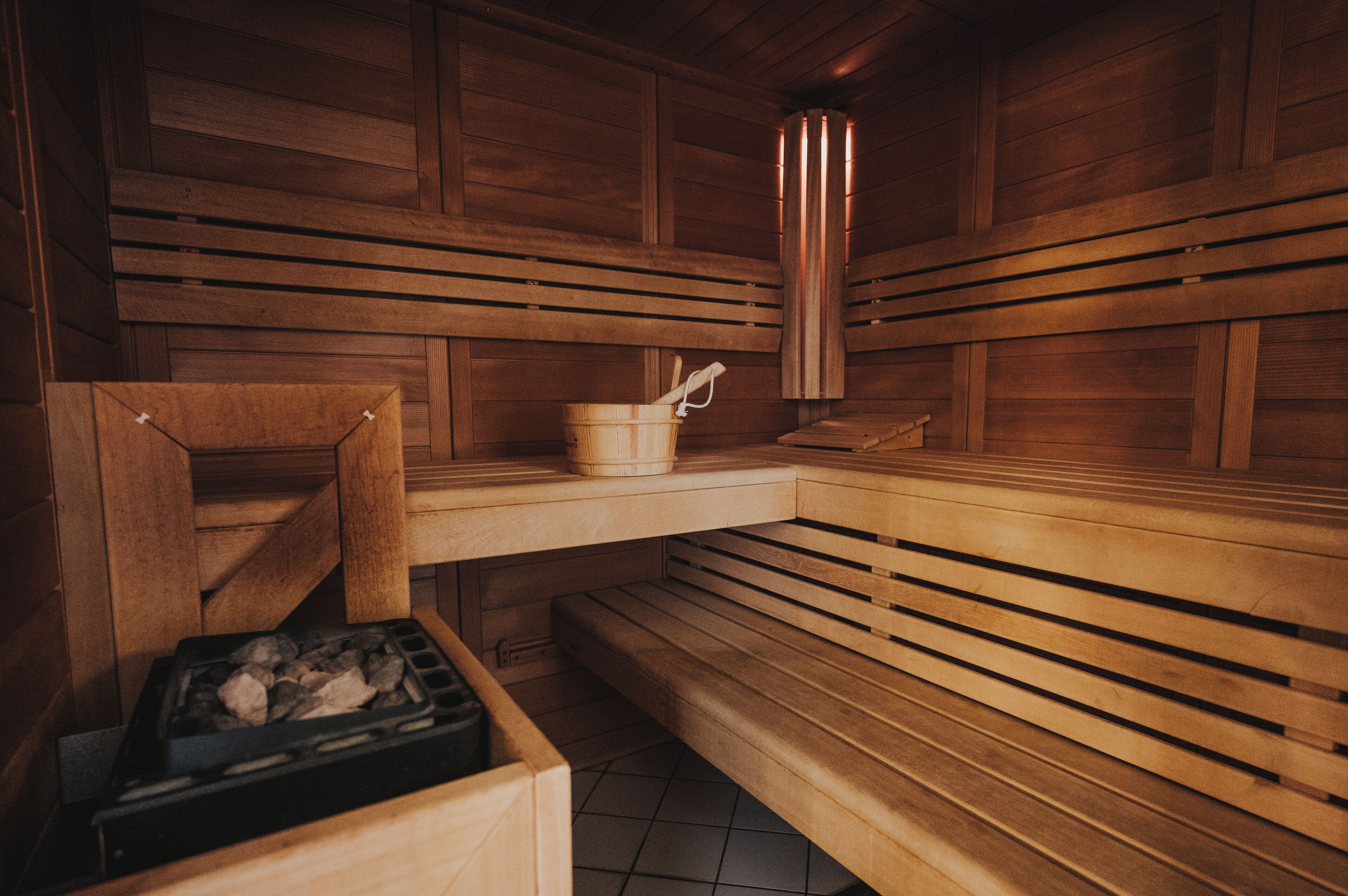 A wooden sauna with benches, a bucket, and a heater.