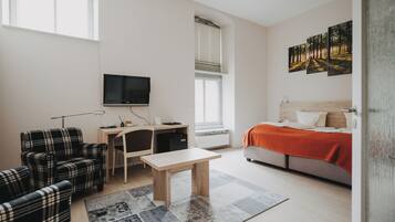 A modern bedroom with a bed, a desk, a chair, a TV, and artwork on the wall.