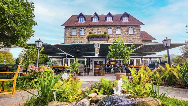 A stone building with a red-tiled roof, outdoor seating, and a garden with rocks and plants. - Hotel Landhaus Schieder (Schieder-Schwalenberg)
