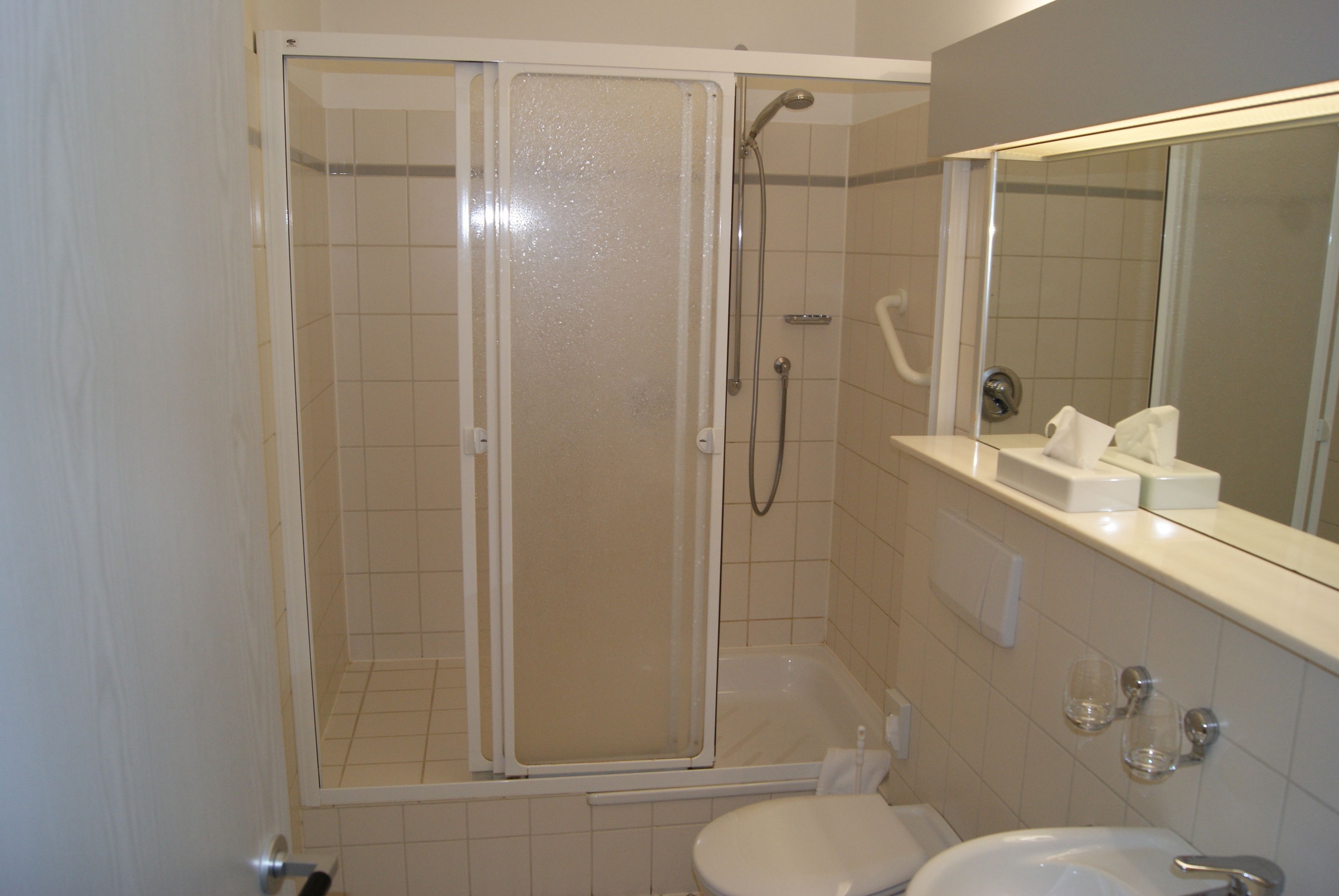 Une salle de bain comprenant un espace douche, des toilettes, un lavabo et un miroir.