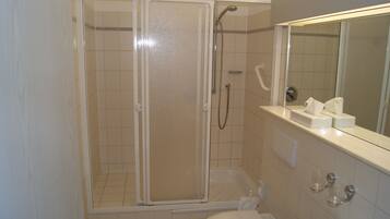 Une salle de bain comprenant un espace douche, des toilettes, un lavabo et un miroir.