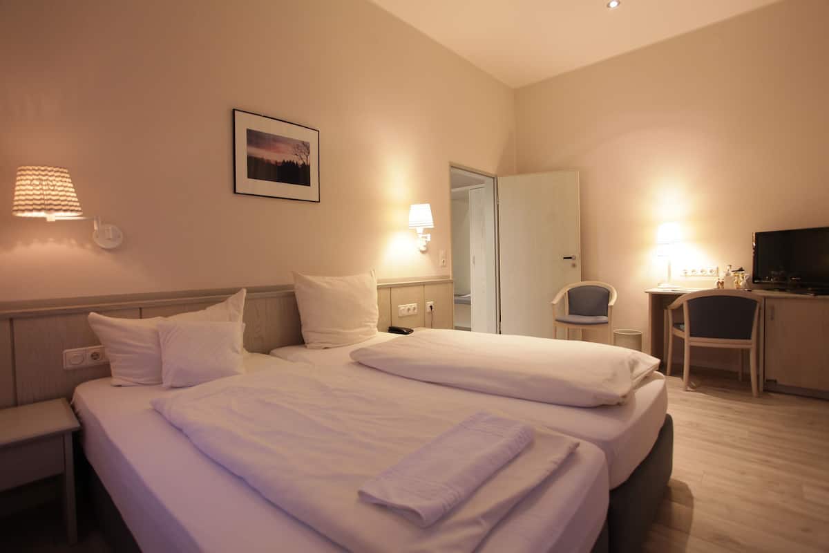 A hotel room with two beds, a desk, a chair, a TV, and a door leading to another room.