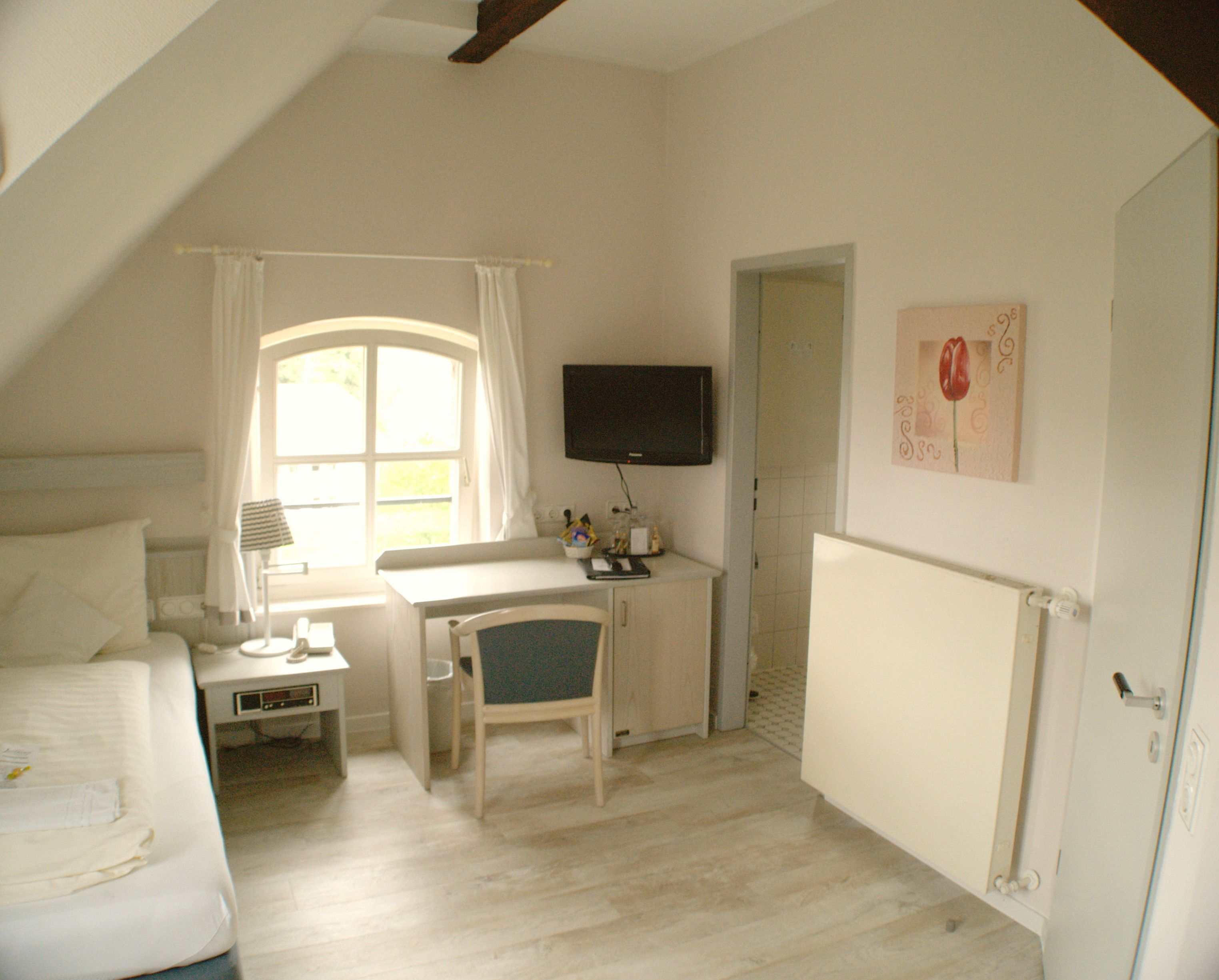 Une chambre à coucher avec un lit, un bureau, une chaise, un téléviseur et une fenêtre avec des rideaux.